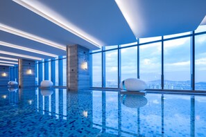 A modern indoor swimming pool with a clear view of the city skyline through large windows. - Jinmao Grandee Hotel Jiangyin Chengfa (Wuxi)