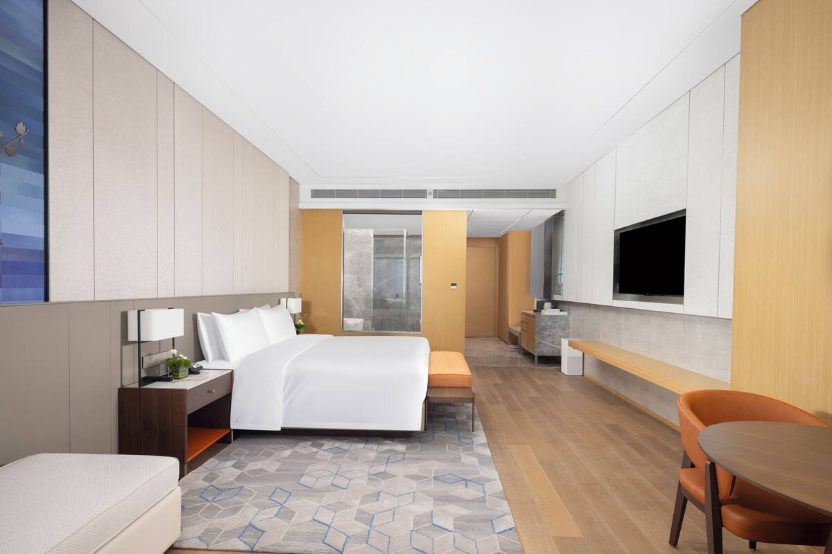 A modern hotel room with a large bed, a desk, a chair, and a TV mounted on the wall.