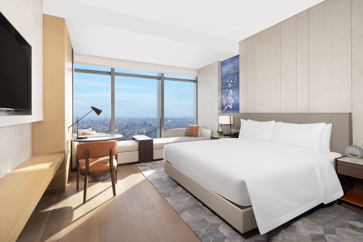 A modern hotel room with a large bed, a desk, and a view of the city.
