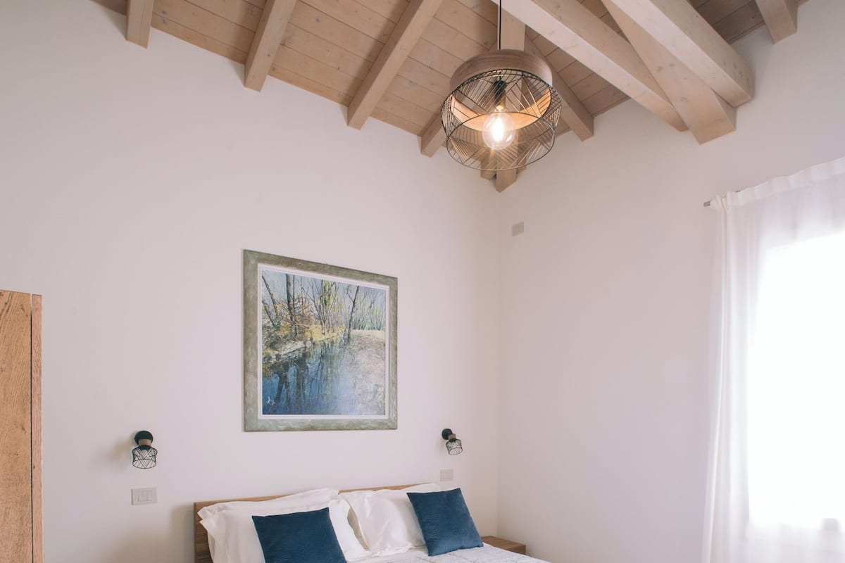 Une chambre avec un plafond en bois, un lit avec une literie blanche et bleue, un tableau au mur et une table de chevet.