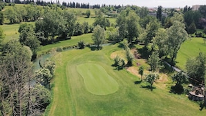 A golf course with a water body, trees, and buildings in the background. - Locanda Golf Musella (San Martino Buon Albergo)