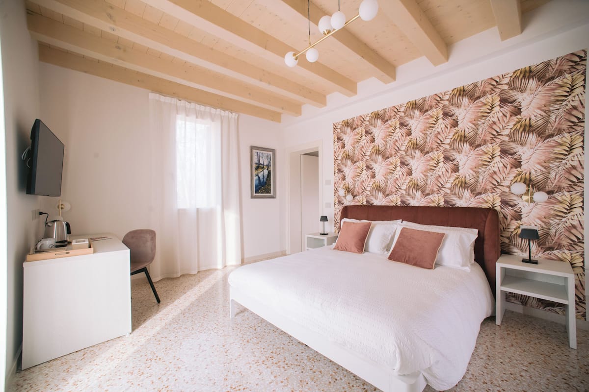 Une chambre à coucher avec un grand lit, un bureau, une chaise, un téléviseur et un mur orné d’un motif de feuilles.