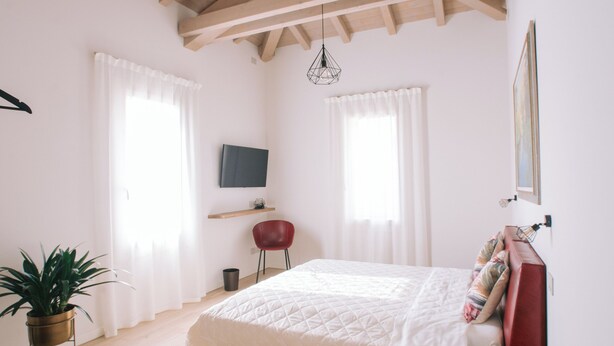 A bedroom with a wooden ceiling, a bed, a TV, a red chair, and a wooden bench. - Locanda Golf Musella (San Martino Buon Albergo)