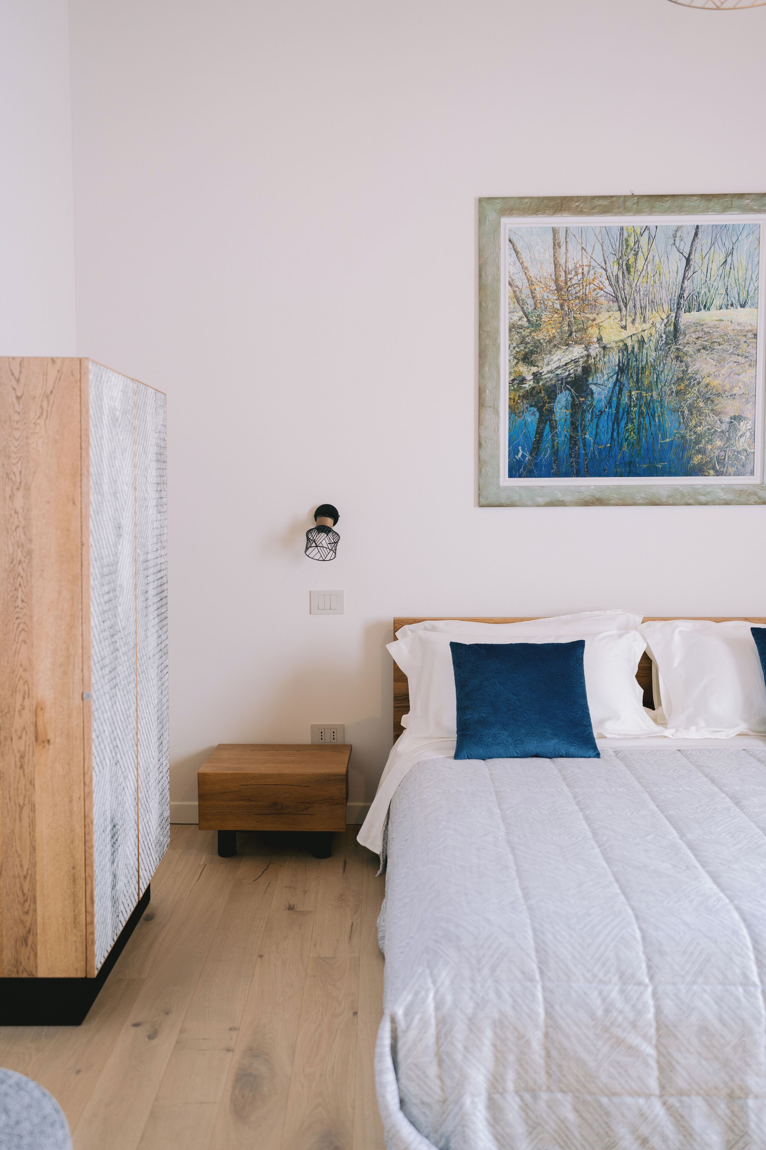 Une chambre à coucher avec un lit, une armoire en bois, une table de chevet et un tableau accroché au mur.
