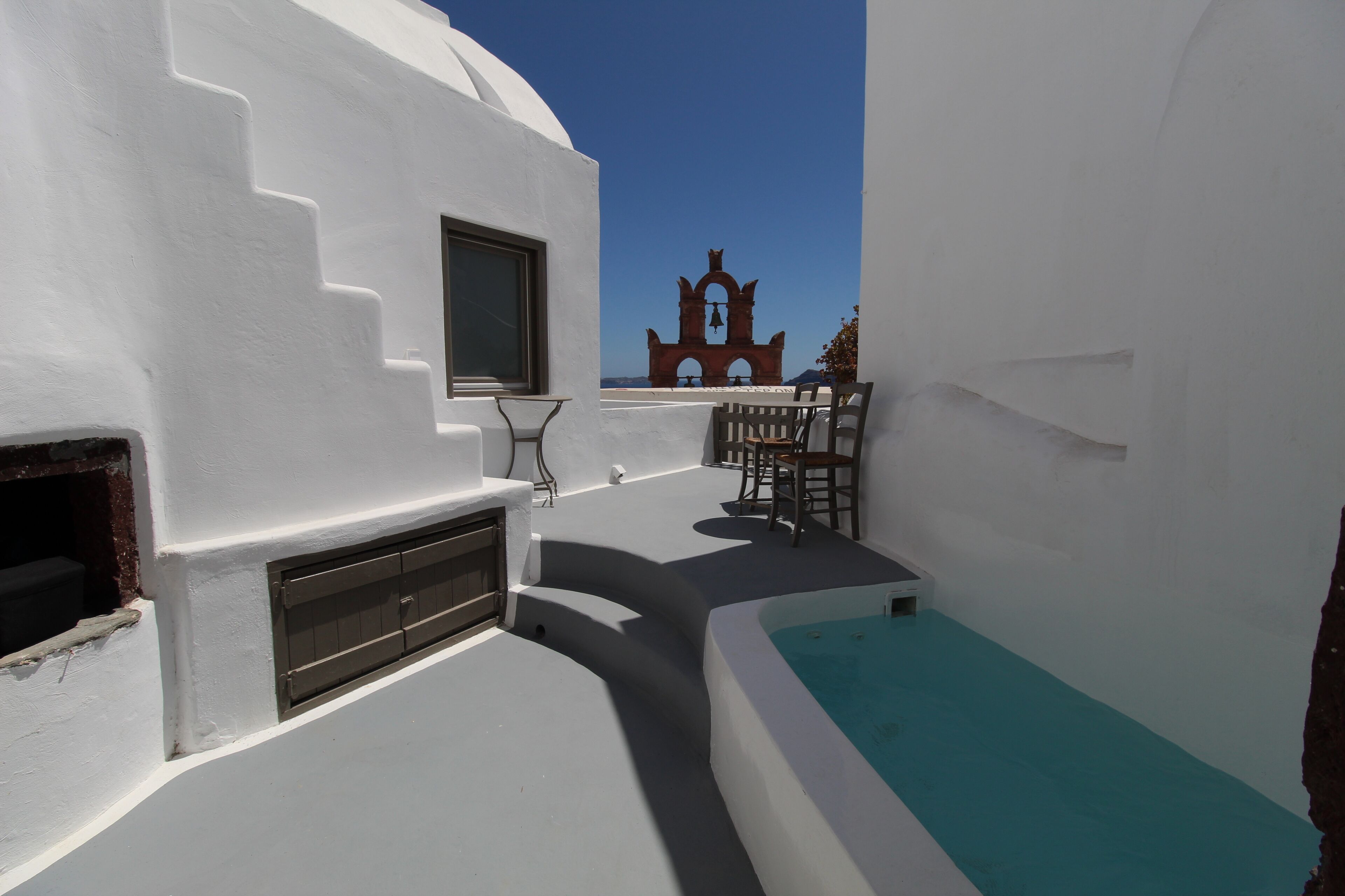Un bâtiment aux murs blancs, doté d’une petite piscine et d’un espace extérieur aménagé pour s’asseoir.