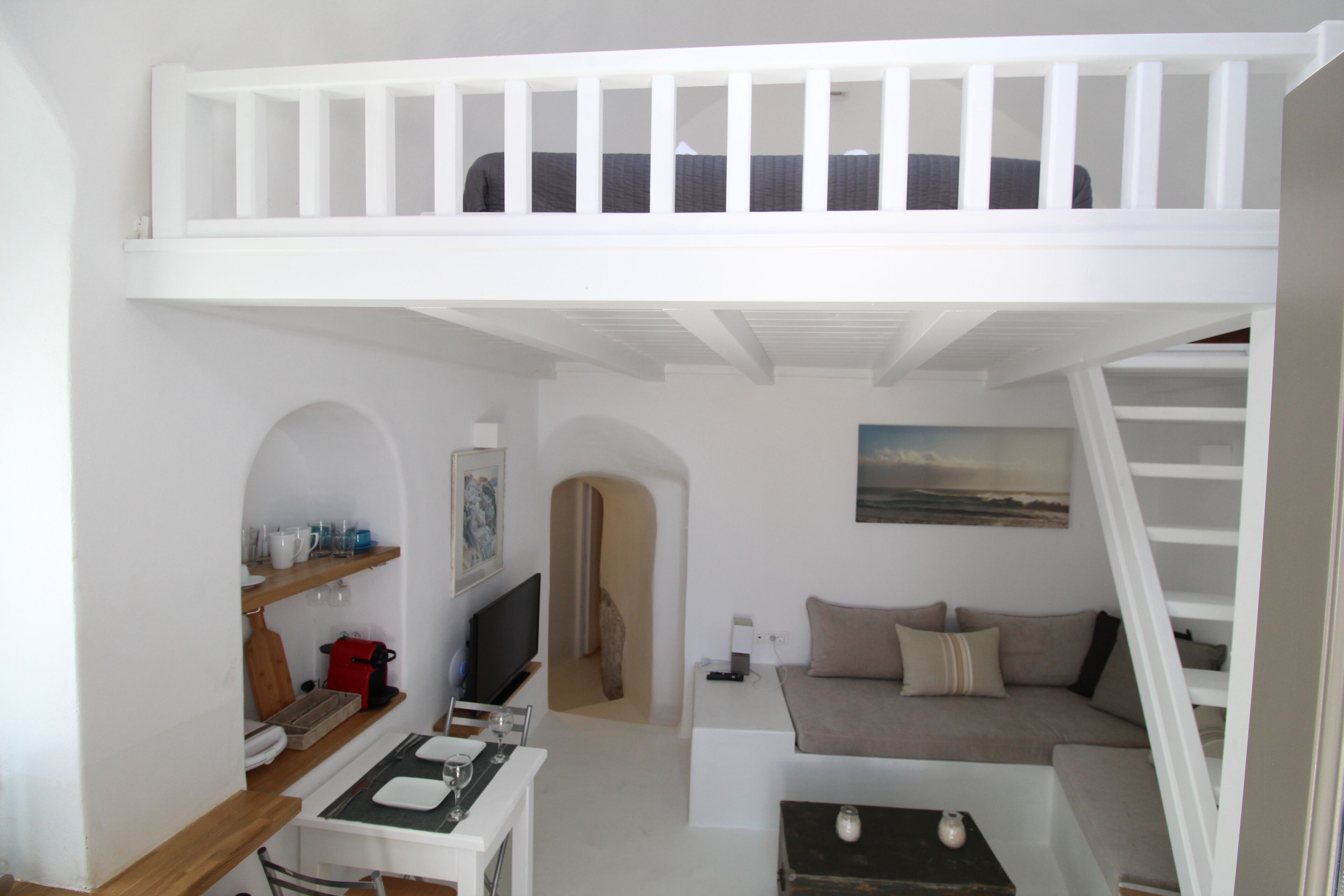 A compact living space with a loft bed, a sofa, a dining area, and a TV.