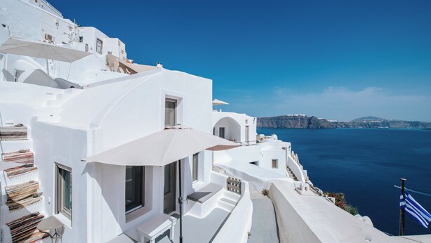 Edifici blanc amb un balcó que dona a un cos d'aigua i una costa llunyana.