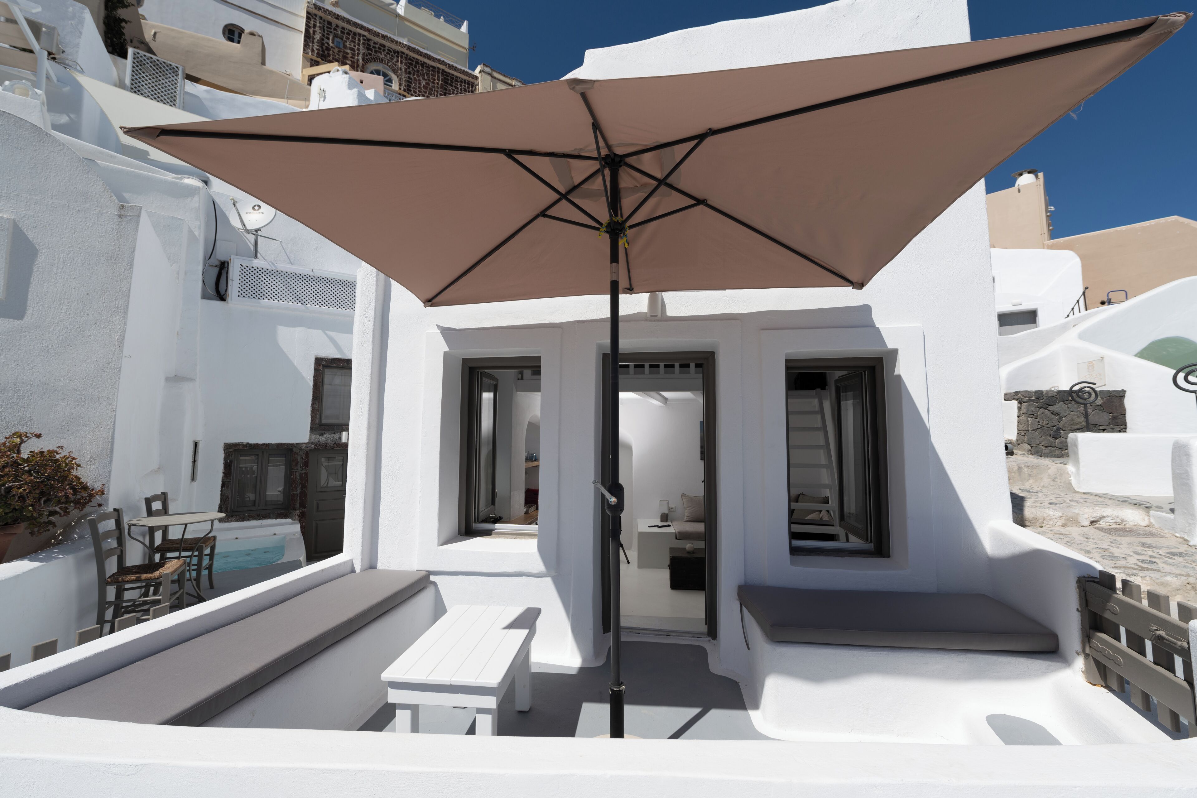 Ein weißes Gebäude mit Balkon, Tisch, Stühlen und einem großen Sonnenschirm.