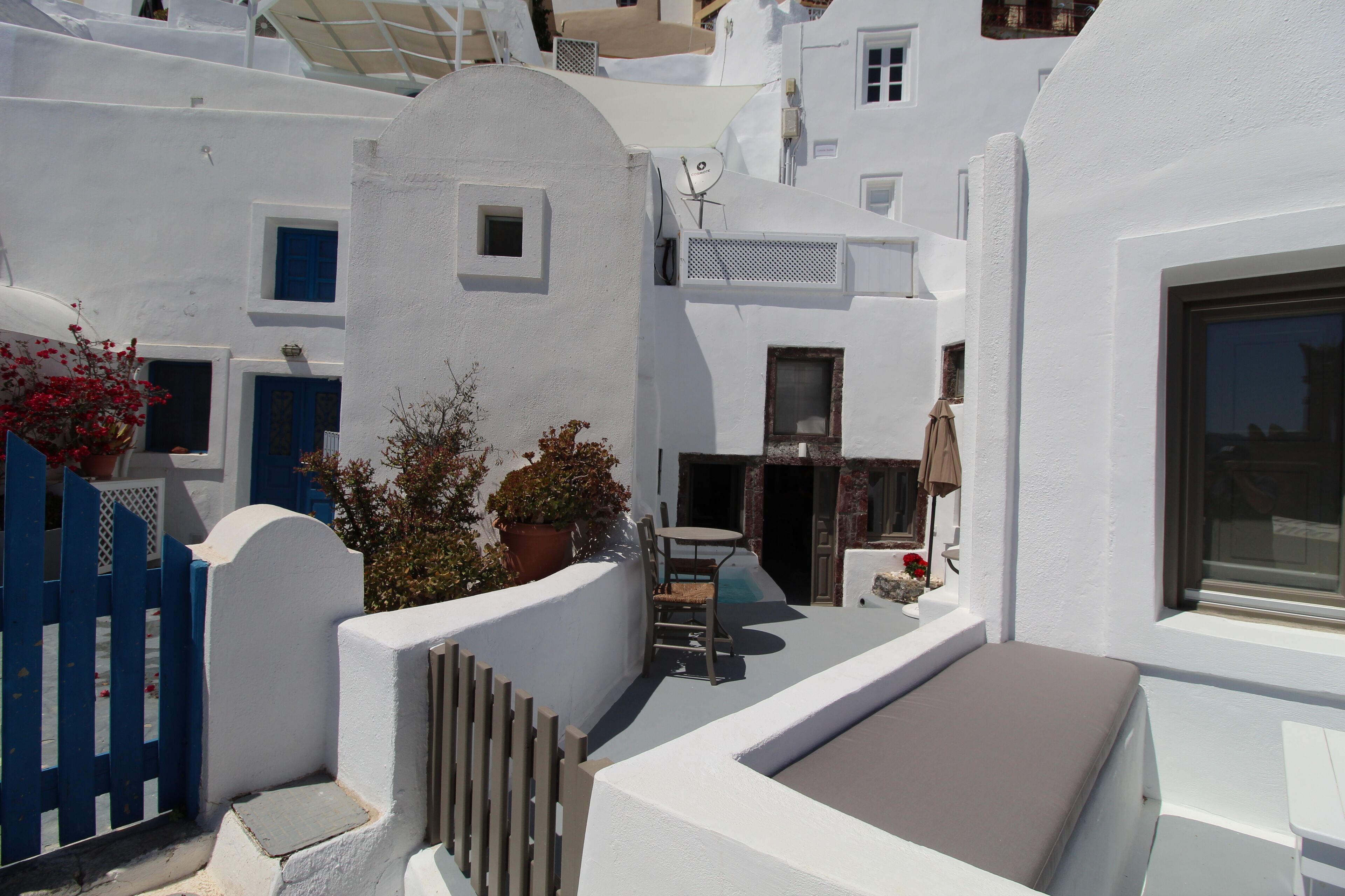 A white-walled building with a small outdoor seating area, a blue gate, and potted plants.