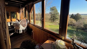 A cozy cabin room with large windows, a hammock, and a view of the countryside.