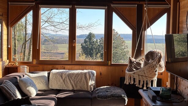 A cozy cabin interior with a large window offering a scenic view, a comfortable sofa, and a hanging chair.
