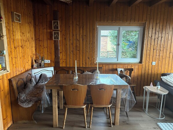 A wooden-paneled room with a dining table, chairs, a bench, and a window.