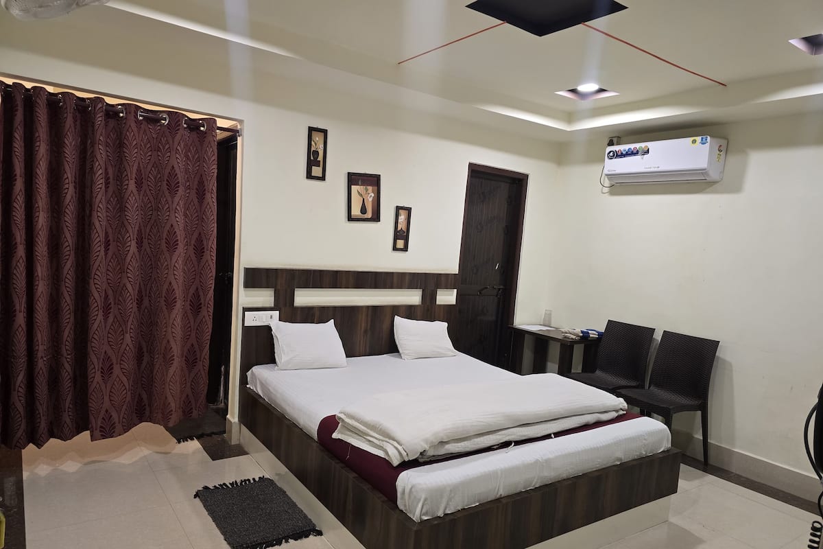 A hotel room with a bed, a desk, and an air conditioning unit.