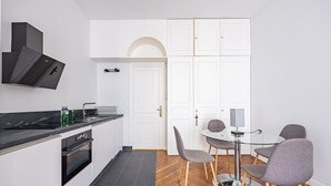 A compact kitchen with modern appliances, a dining area with a glass table and chairs, and a white door with a keyhole.