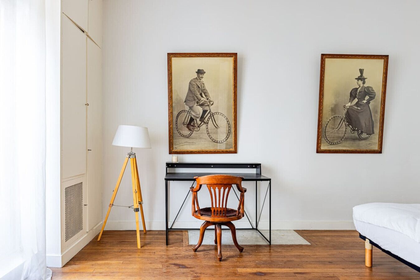 Ein Zimmer mit Holzboden, einem Schreibtisch mit Lampe, einem Stuhl und zwei gerahmten Bildern an der Wand.