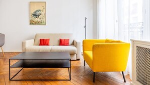 A living room with a sofa, a yellow armchair, a black coffee table, and a painting on the wall.