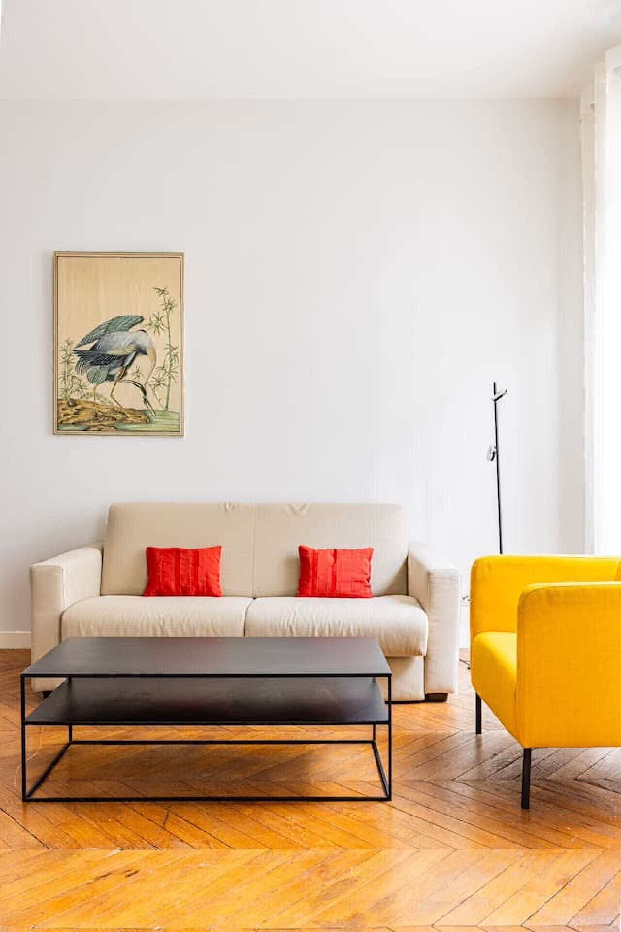 Un salón moderno con un sofá, cojines rojos, una mesa de centro negra, un sillón amarillo y un cuadro en la pared.