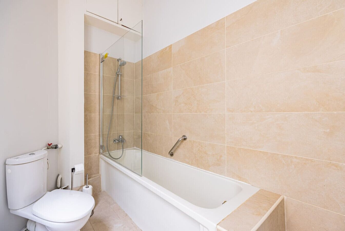 Et badeværelse med toilet, glasvæg omkring brusebad og badekar.