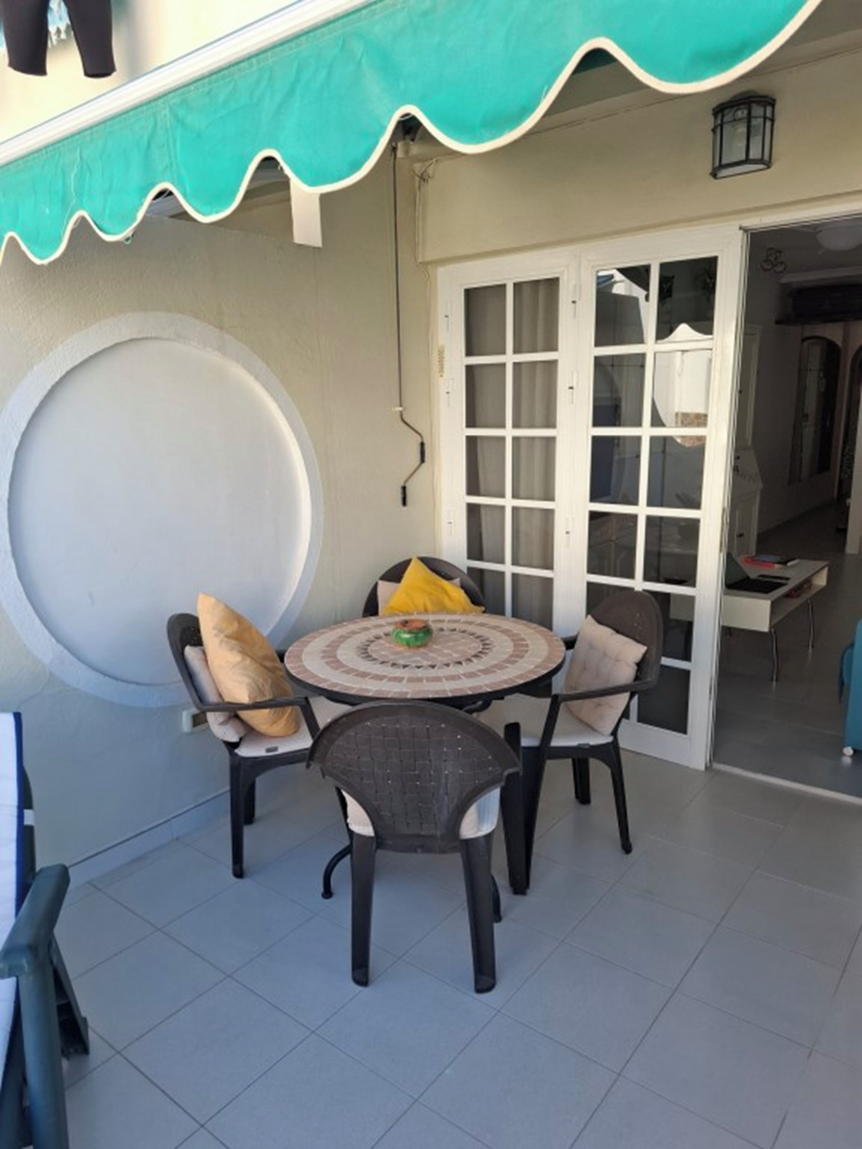 Eine Terrasse mit einem runden Tisch und vier Stühlen, ein großes Fenster und eine Tür zu einem Innenraum.