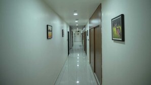 A long, narrow hallway with white walls and a shiny tiled floor. - Hotel Aagman (Palanpur)