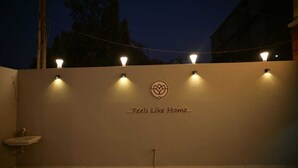 A wall with four wall-mounted lights and a logo with the text "Feels Like Home...". - Hotel Aagman (Palanpur)