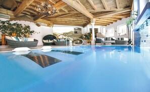 An indoor swimming pool with wooden beams, a chandelier, and a spa area with seating. - Hotel Eichingerbauer (Sankt Lorenz)
