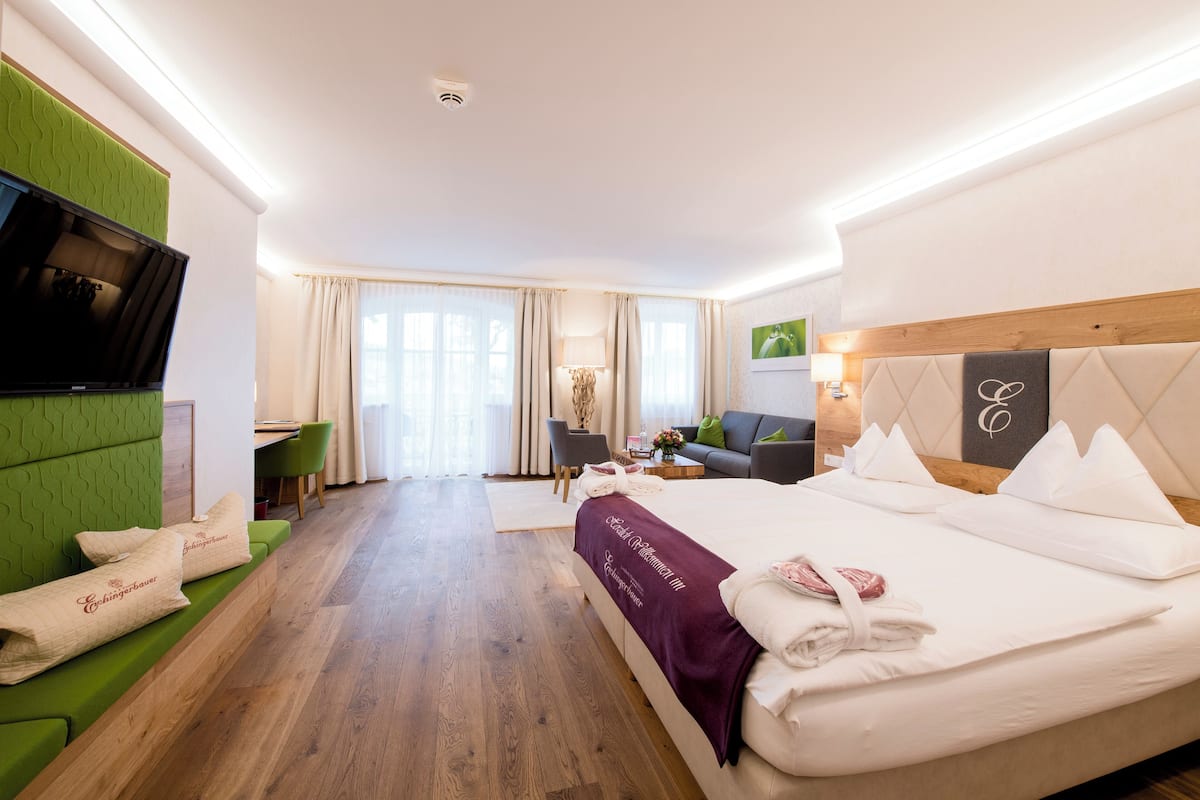 Hotelkamer met een groot bed, een groene bank, een televisie en een eethoek op de achtergrond.