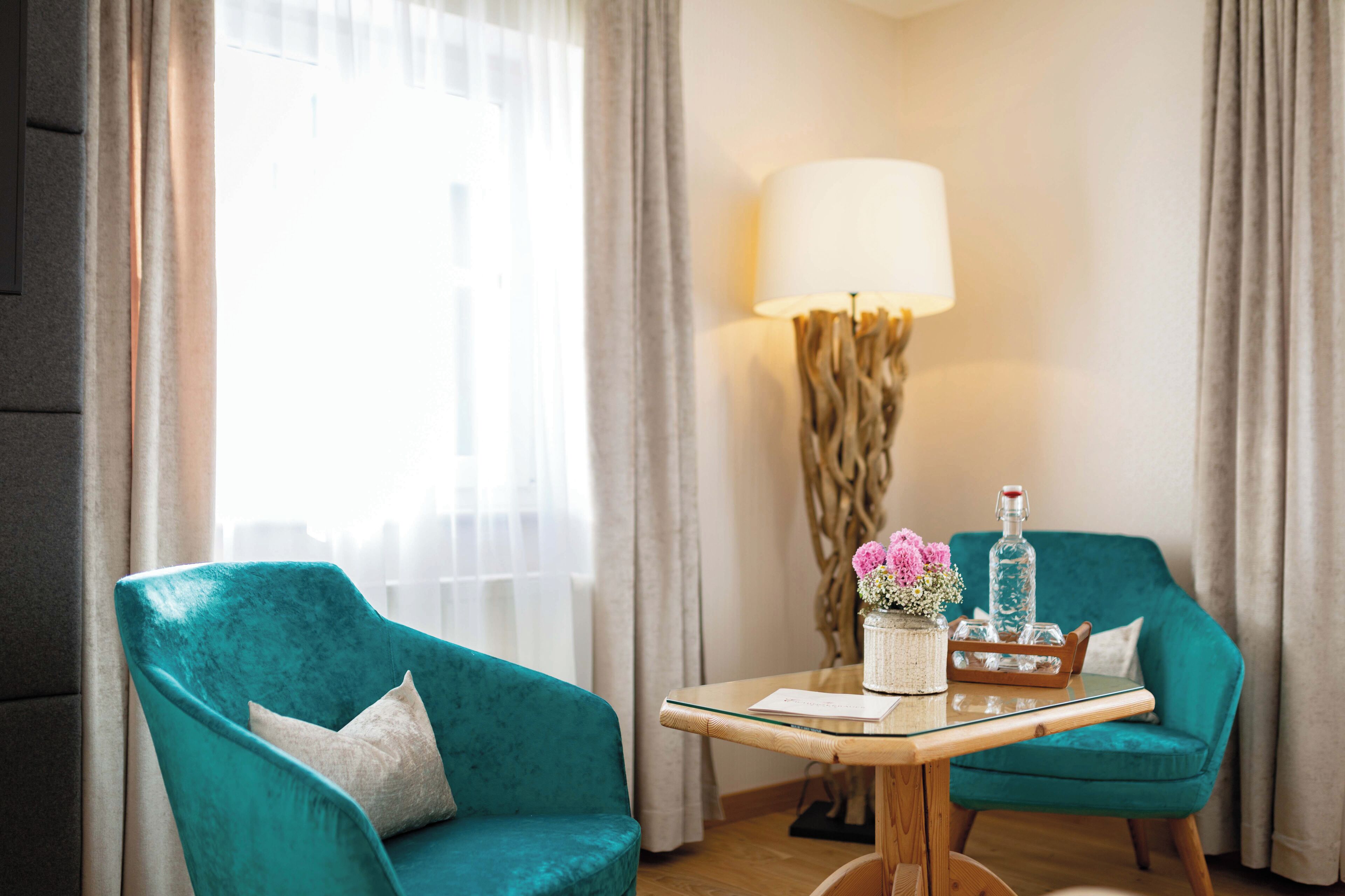 A teal armchair, a small table with a lamp, and a vase with flowers.