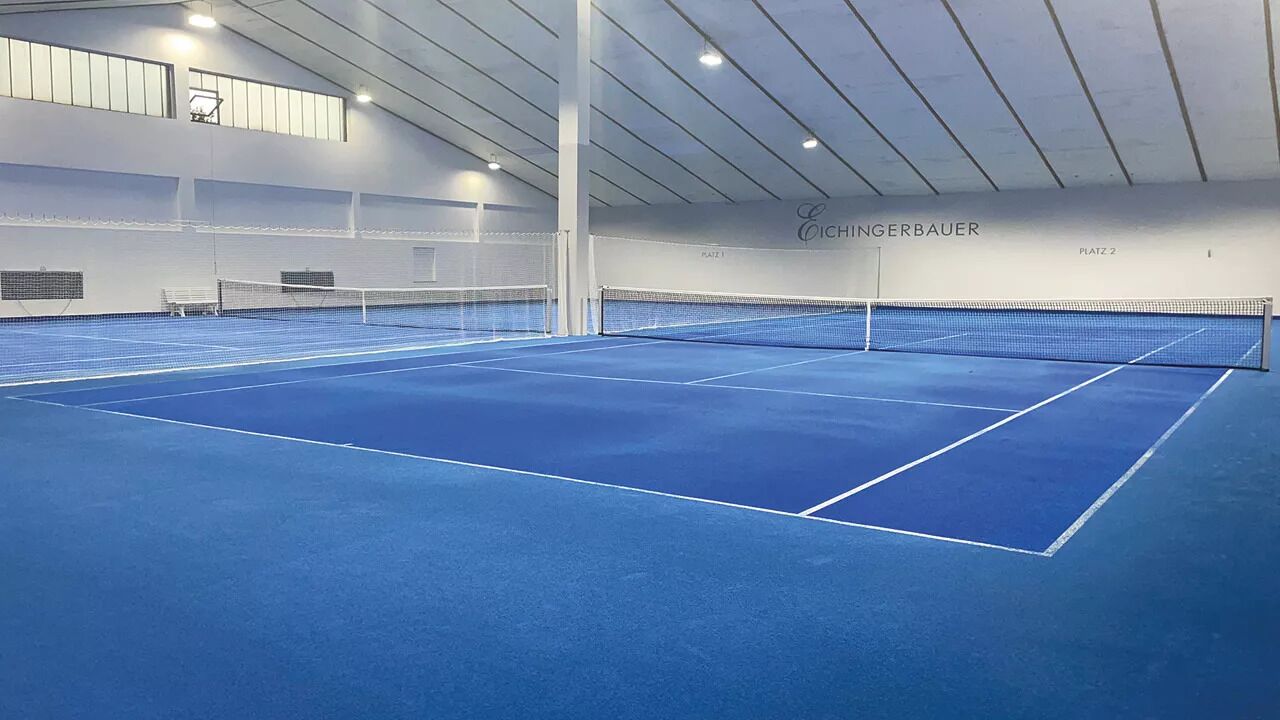 An indoor tennis court with a blue surface, net, and white walls.