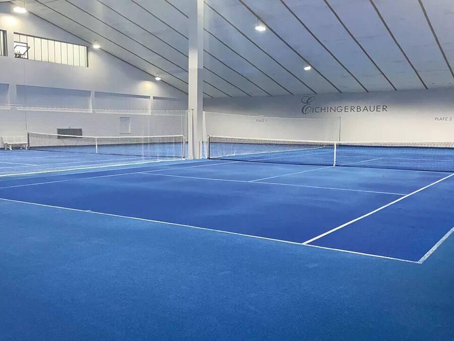 An indoor tennis court with a blue surface, net, and white walls.
