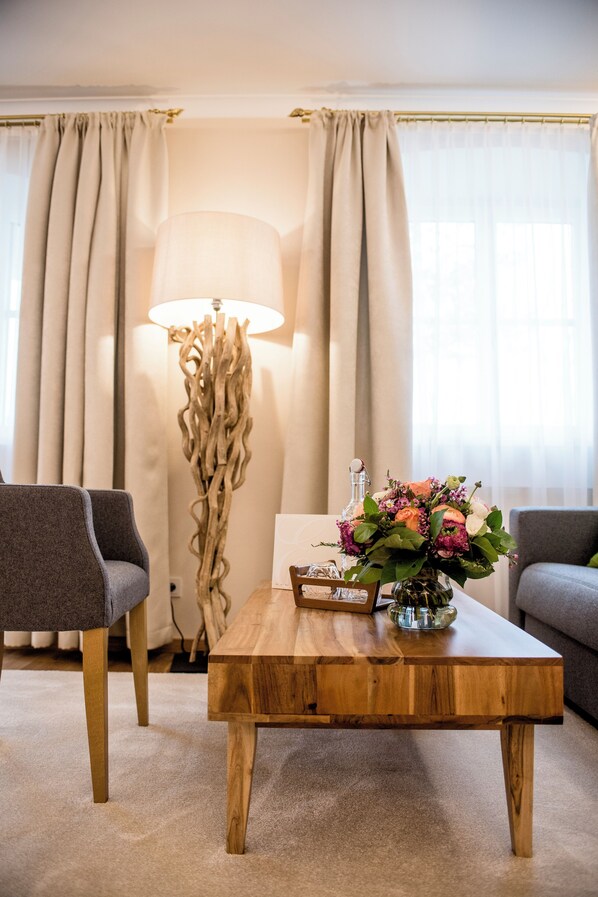 A modern living room with a wooden coffee table, two grey armchairs, a floor lamp, and a vase of flowers. - Hotel Eichingerbauer (Sankt Lorenz)