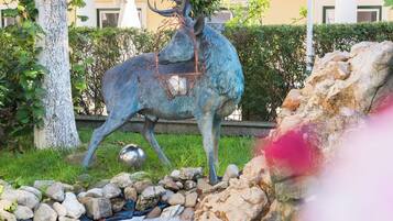 A statue of a deer with antlers and a basket, surrounded by rocks and a small stream.