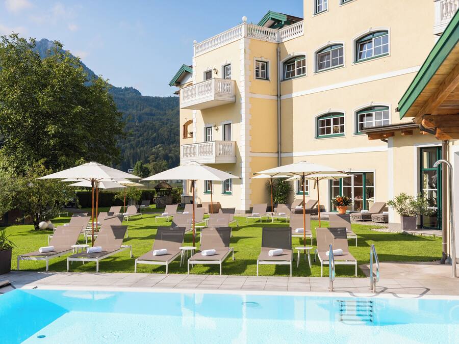 A hotel with a swimming pool, sun loungers, and umbrellas.