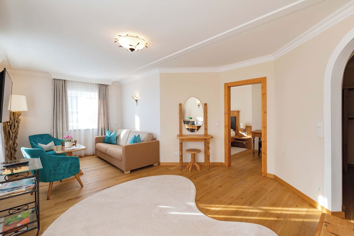 Een moderne woonkamer met een bank, smaragdgroene fauteuils, een bijzettafeltje en een houten vloer.