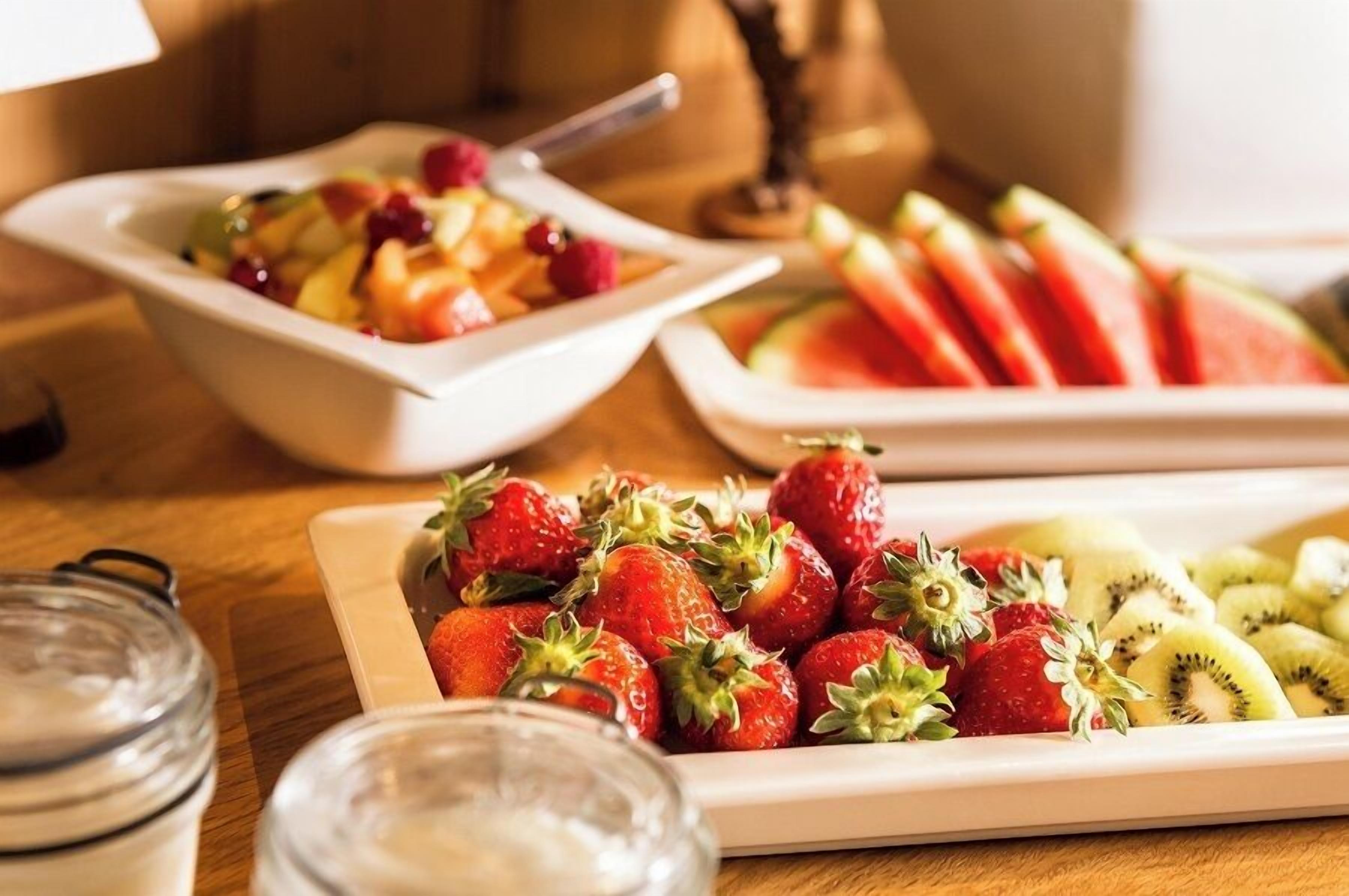 Une table sur laquelle on trouve différents fruits, notamment des fraises, des kiwis et des tranches de pastèque.