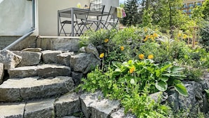 Un jardin avec un escalier en pierre, une table entourée de chaises et un bâtiment en arrière-plan.