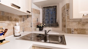 A modern kitchen with a double sink, white cabinets, decorative tiles, and a window with blue curtains. - Beautiful private villa for 4 people with WIFI (Cervo)