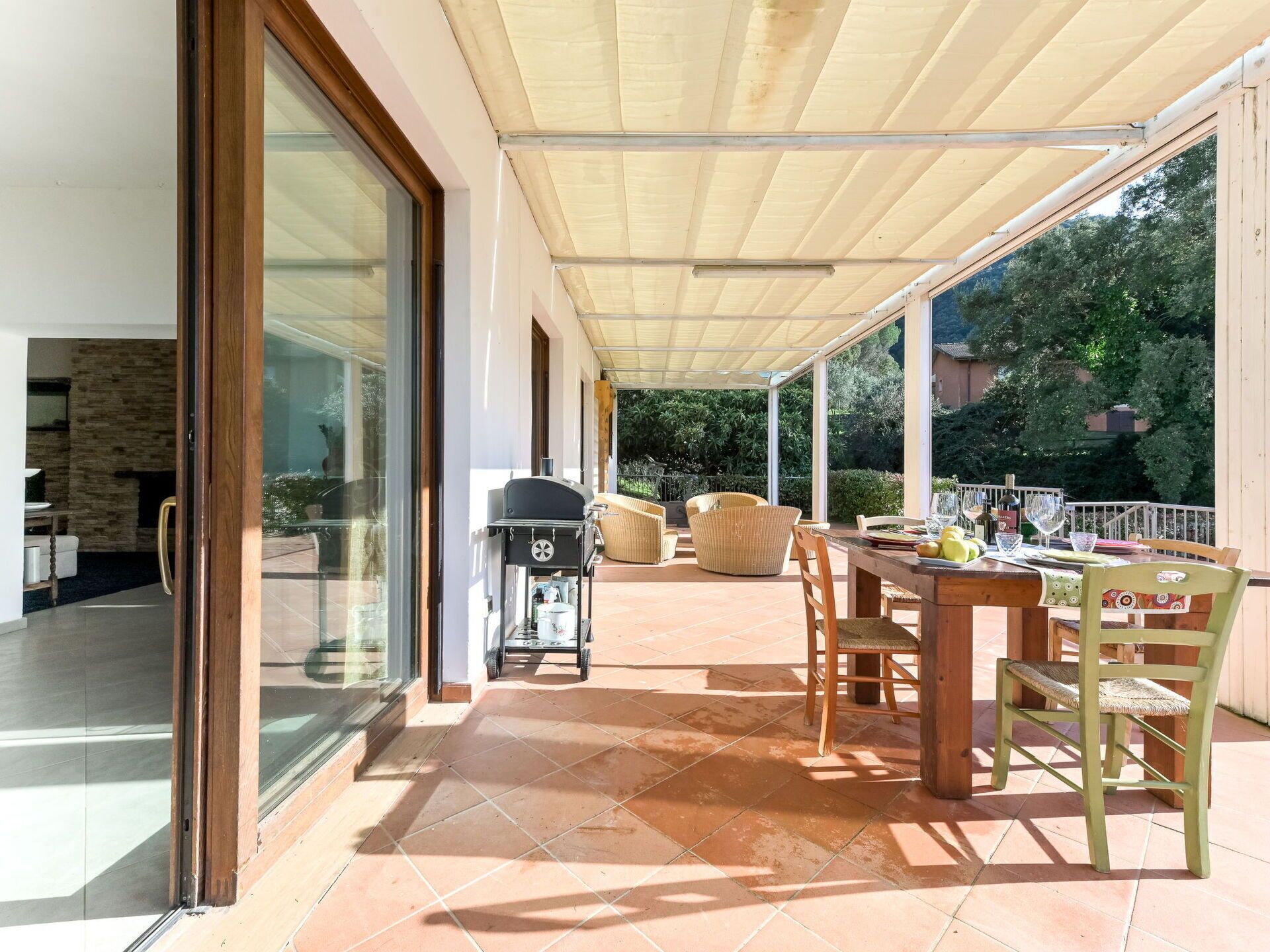 A covered patio with a dining table and chairs, a grill, and a view of the surrounding greenery.