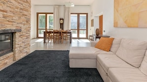 A modern living room with a stone fireplace, a dining area with a wooden table and chairs, and a large window offering a view of greenery. - Stunning private villa for 7 people with WIFI, private pool, patio, pets allowed and panoramic v... (Scarlino)