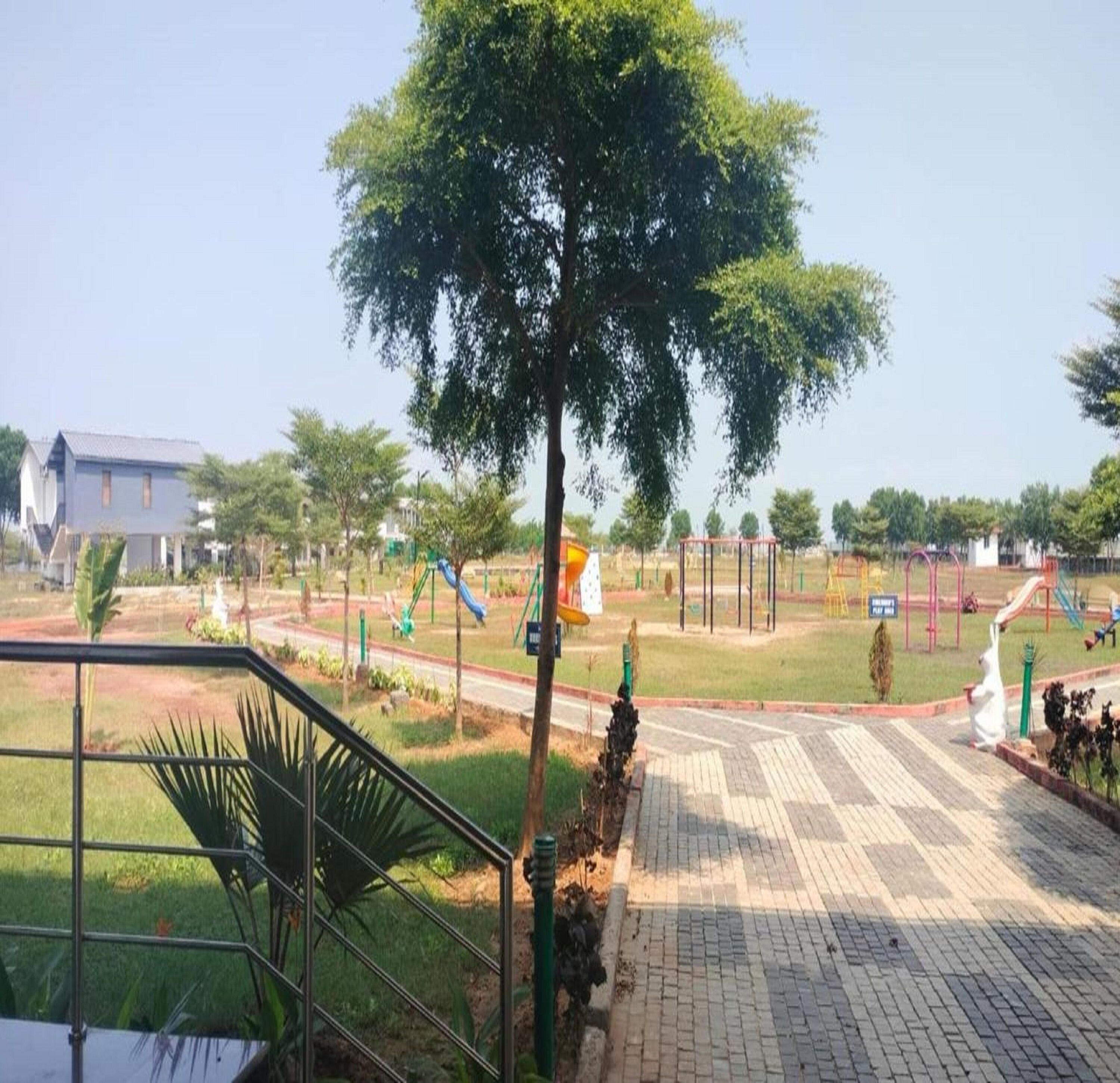 Un parque con juegos infantiles, un sendero pavimentado y un edificio al fondo.