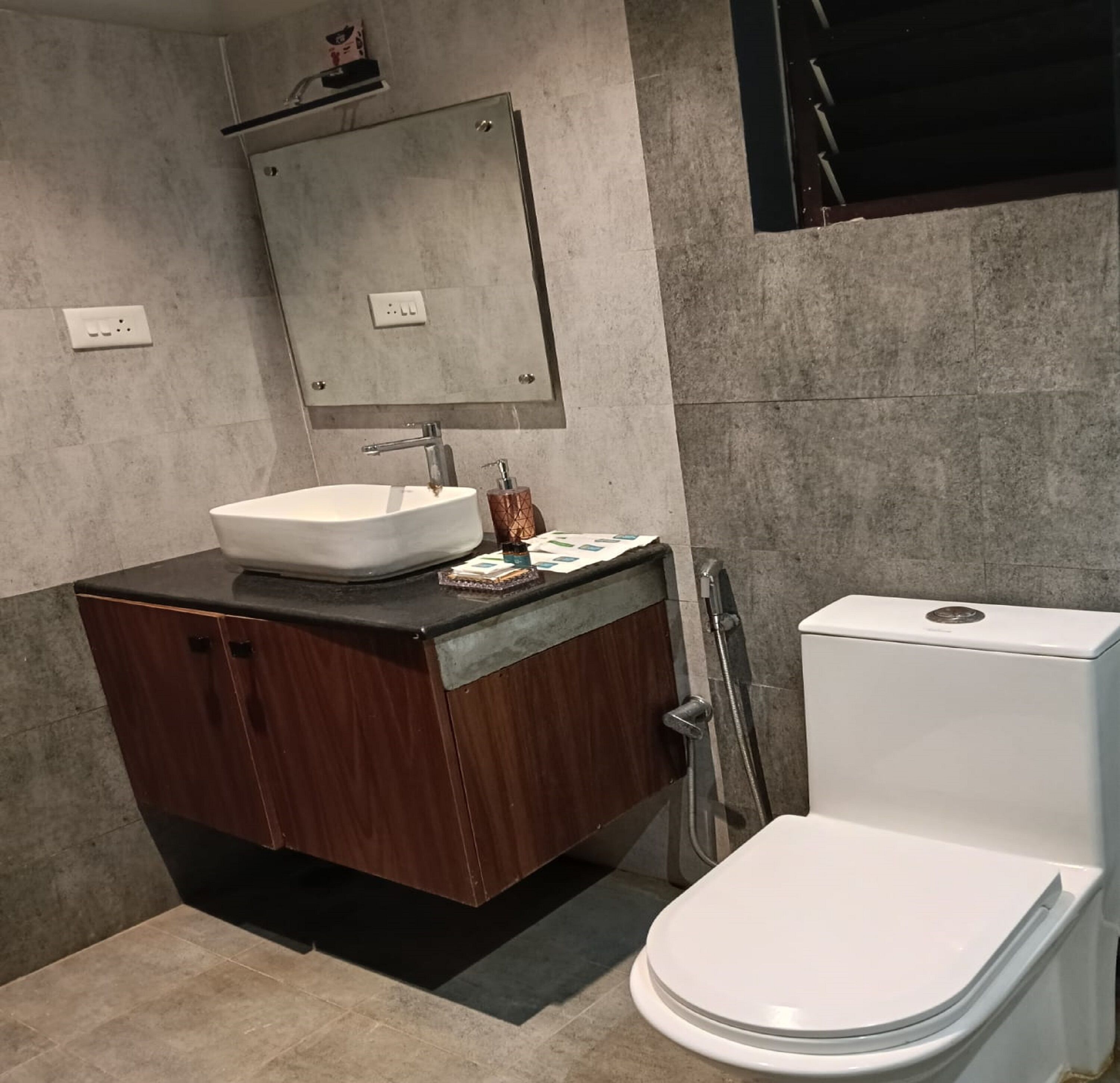 Ein modernes Badezimmer mit einem weißen Waschbecken, einer dunklen Holz-Kommode, einem Spiegel über dem Waschbecken und einer weißen Toilette.