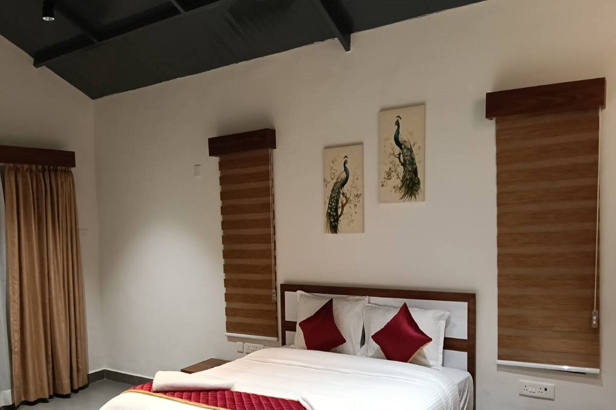 Une chambre à coucher avec un lit en bois, du linge de lit blanc et deux fenêtres fixées au mur, équipées de rideaux.