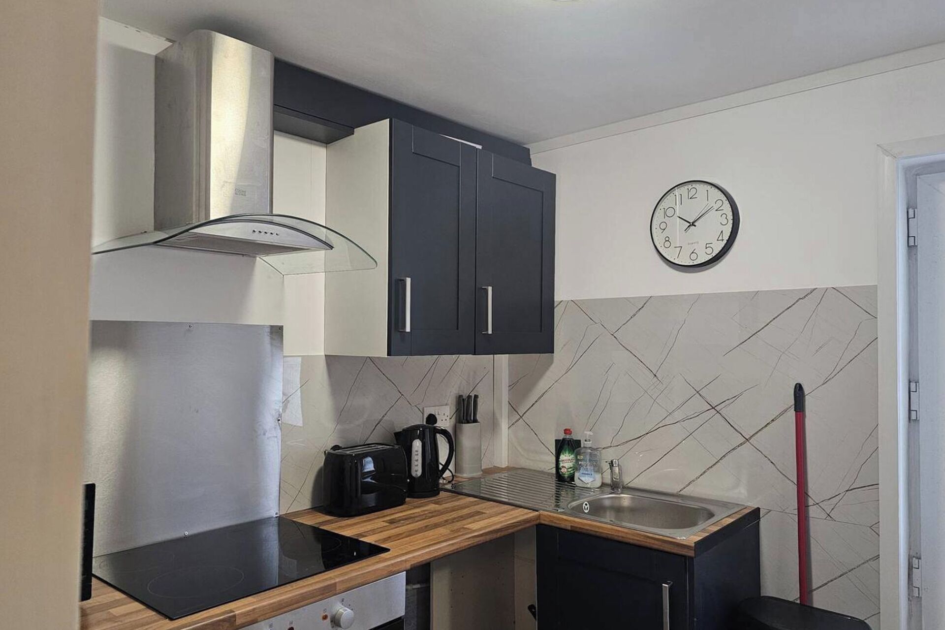 A compact kitchen with a built-in stove, a coffee maker, and a clock on the wall.