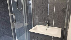 A modern bathroom with a glass-enclosed shower, a white sink, and dark marble walls.