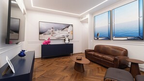 A modern living room with a large window, a brown leather sofa, a blue cabinet, and a wooden herringbone floor. -  Italianway - XXV Aprile 7 B - Smeraldo (Milan)