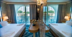 A hotel room with two beds, a central table, and large windows with curtains.