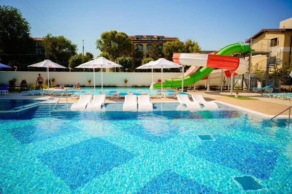 A swimming pool with a water slide, lounge chairs, and umbrellas.