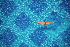 A person swimming in a clear blue pool with a geometric tile pattern.