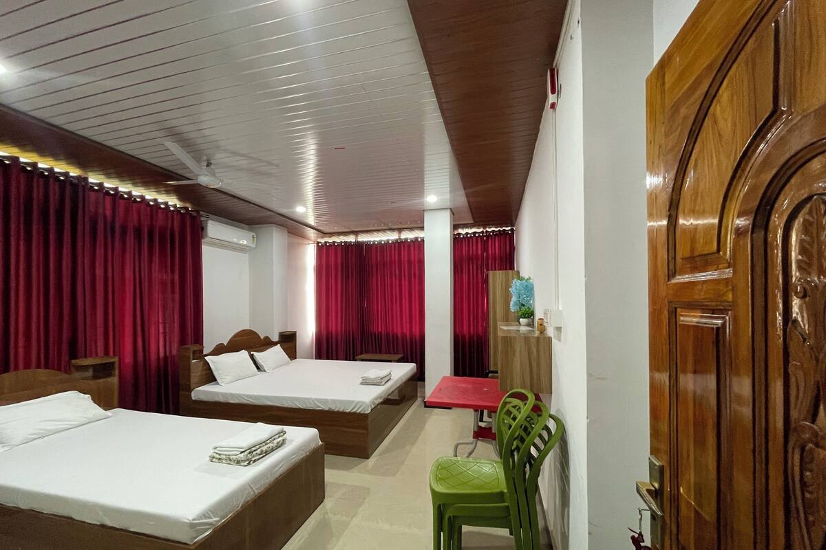 A hotel room with two beds, a desk, a chair, and a wooden door.