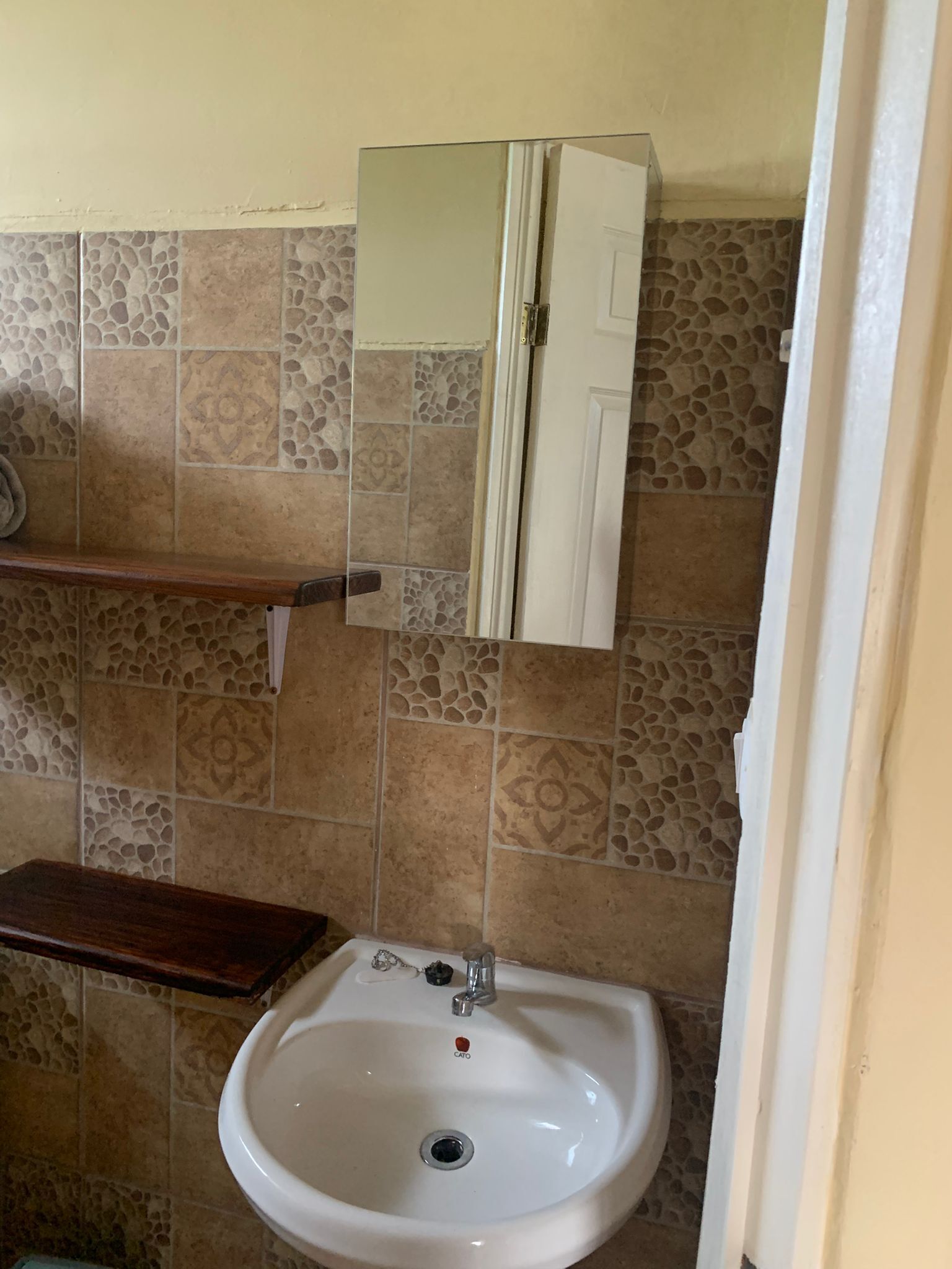 Ein Badezimmer mit einem weißen Waschbecken, einem Spiegel darüber und einer gefliesten Wand mit Muster.